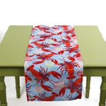 Blue table runner featuring a red lobster and seashell pattern displayed on a green table.