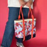 Rock Lobster canvas tote bag with red straps and blue fabric with a repeating lobster and shell motif being held by model