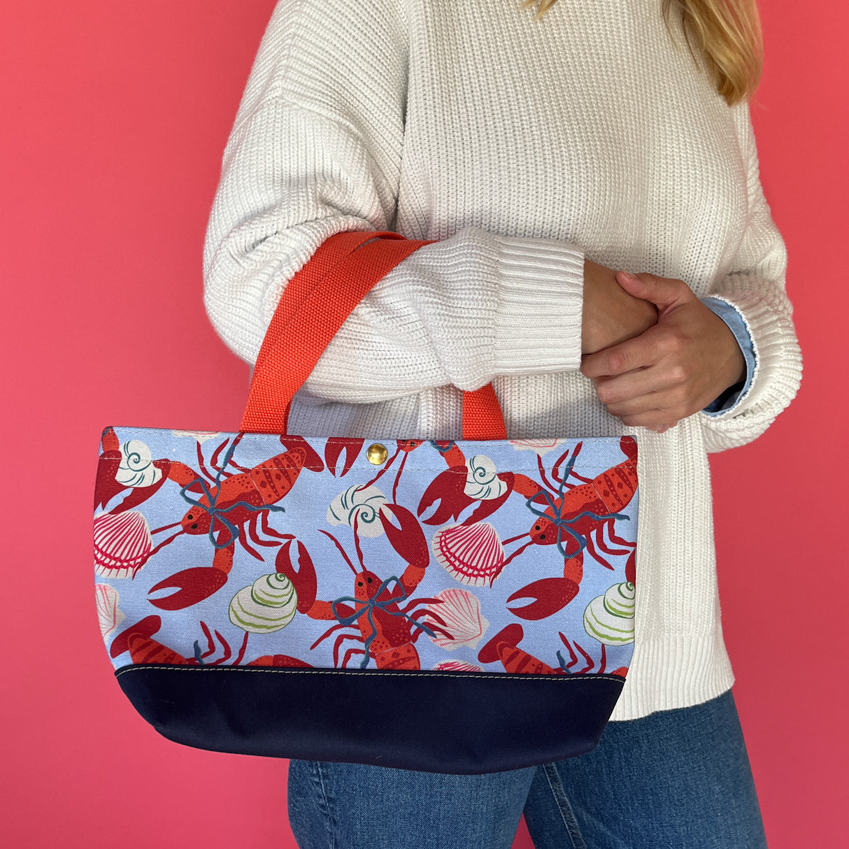 Rock Lobster small canvas tote bag with red straps and blue fabric with a repeating lobster and shell motif on models arm