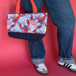 Rock Lobster small canvas tote bag with red straps and blue fabric with a repeating lobster and shell motif hanging by models legs