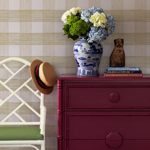 A pink chext, vase of flowers and white chair against a wall of large scale beige gingham wallpaper