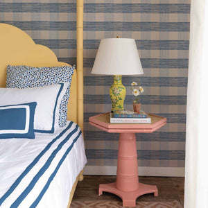 A yellow bed and pink side table against a wall of large scale blue gingham wallpaper