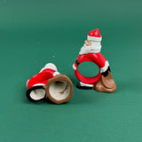 Two ceramic Santa Claus napkin rings on a green background