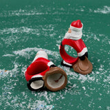 wo Santa Claus-shaped napkin rings on a green surface with faux snow scattered around