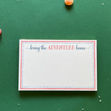 Luxe large notepad with quote ‘Bring the Adventure Home’ in blue and red typography, bordered with dotted design for chic desk stationery. placed in a green background