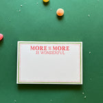 Luxe large notepad with quote ‘More of More is Wonderful’ in red lettering, featuring a dotted border and green trim, perfect for stylish note-taking. placed in a green background