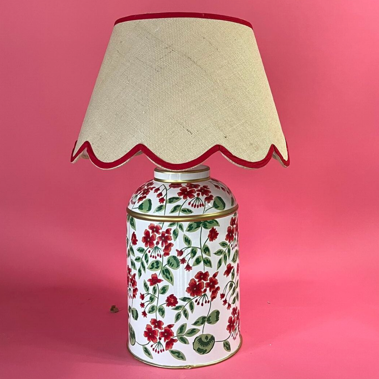 a red, white and green table lamp painted with red geraniums in a pattern called "Cottage Grove" from madcap cottage and a rattan scalloped shade with red trim