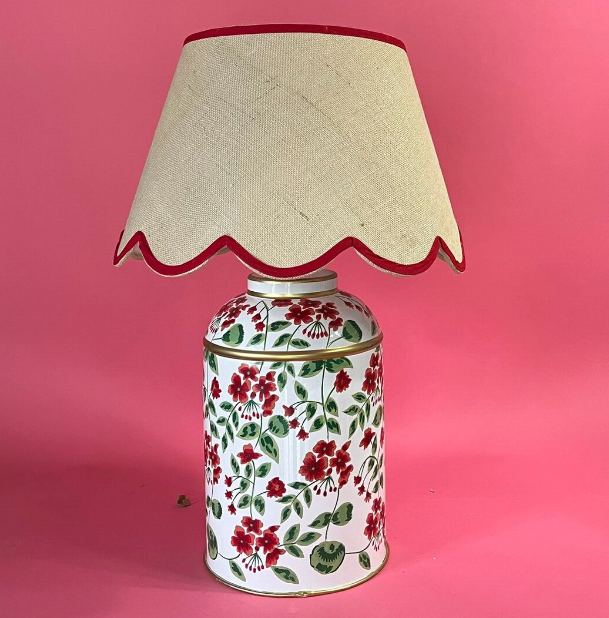 a red, white and green table lamp painted with red geraniums in a pattern called "Cottage Grove" from madcap cottage and a rattan scalloped shade with red trim