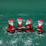 Four Santa Claus-shaped napkin rings standing on a green surface with faux snow scattered around