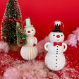 Two sparkly christmas snowman ornaments wearing top hats against a red background with snow and christmas trees.