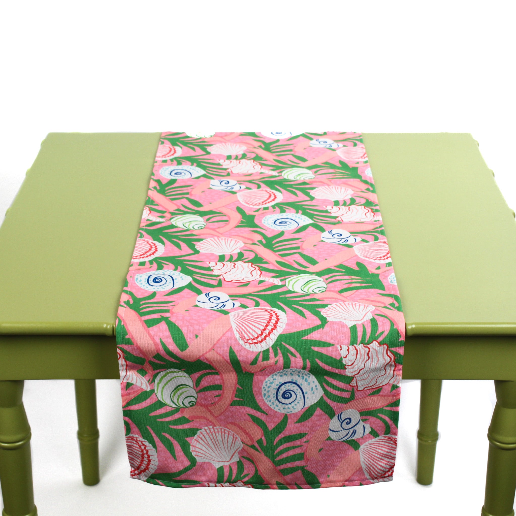 Pink and green table runner featuring colorful seashell patterns laid across a green table.