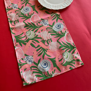 Shell Seekers cloth Table Runner features colorful shells, pink ribbons and green foliage on a pink background