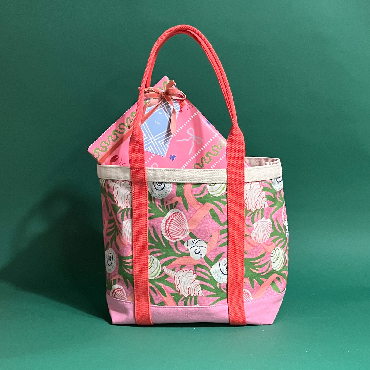 Large Shell Seekers canvas tote bag with pink fabric with a repeating seaweed and shell motif with a present sticking out of bag