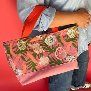 Small Shell Seekers canvas tote bag with pink fabric with a repeating seaweed and shell motif on models arm
