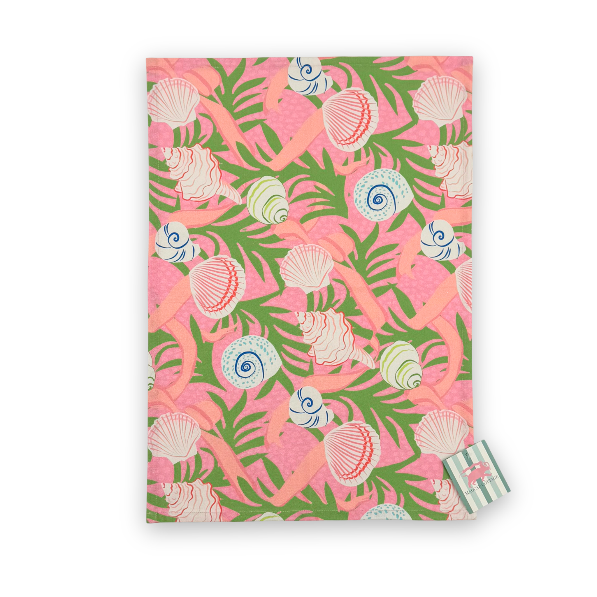 Madcap Cottage Shells and Ribbons cotton tea towel featuring colorful seashells, pink ribbons, and green tropical foliage on a vibrant pink background.
