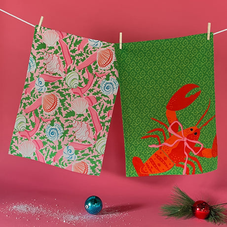 Shells and holly with ribbons on pink background and red lobster on green background tea towels