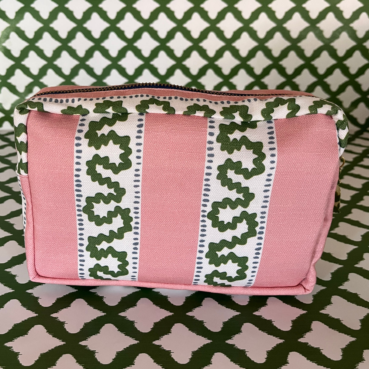 Side view of Harbor Trail toiletry bag in Bahama pink with a green ribbon and blue dash motif.