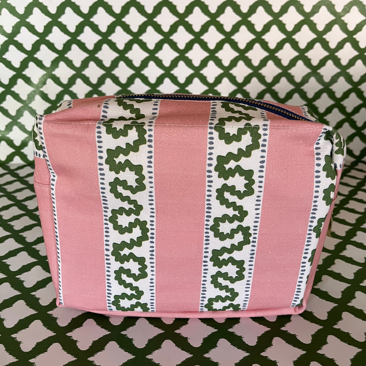 Side view of Harbor Trail toiletry bag in Bahama pink with a green ribbon and blue dash motif.
