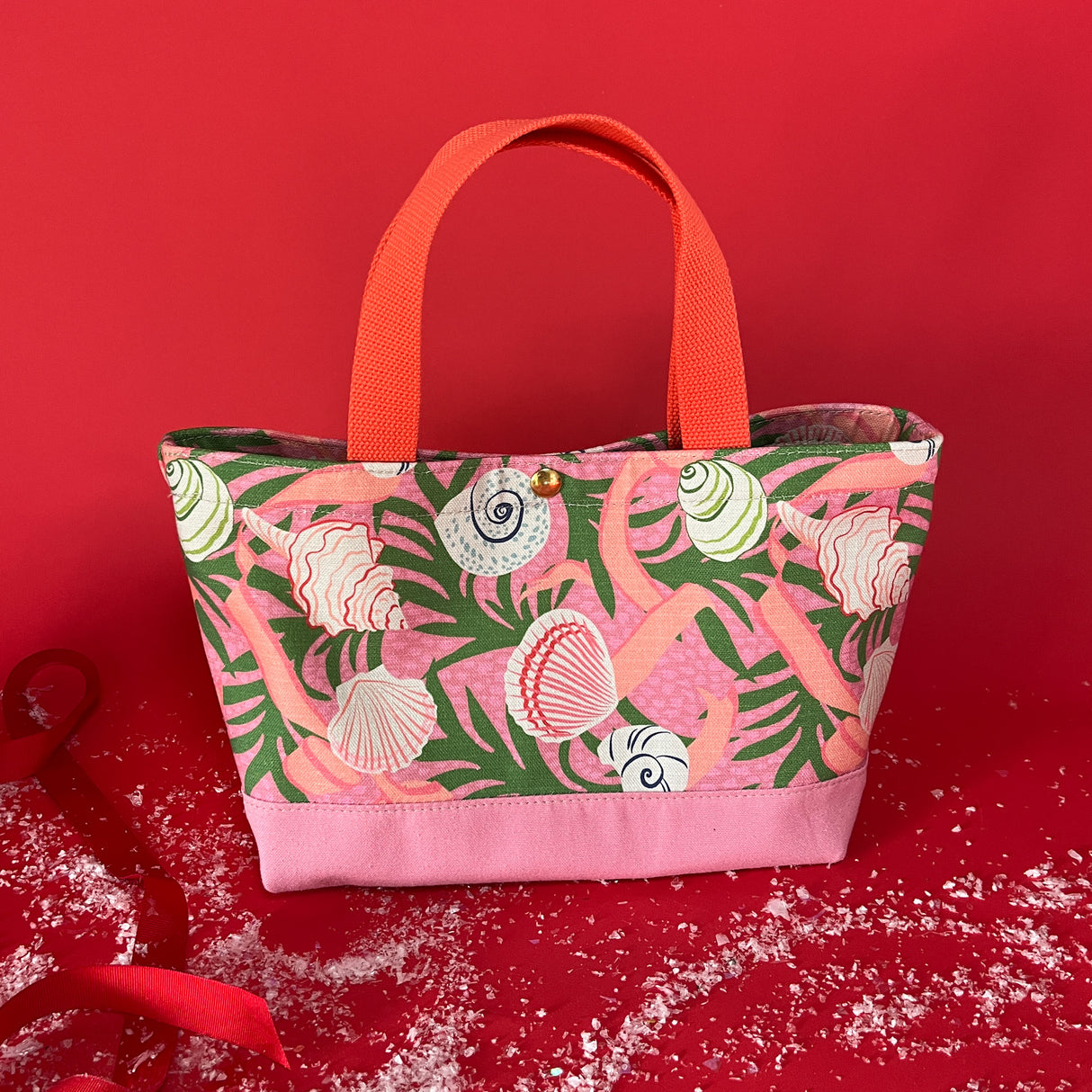 Small Shell Seekers canvas tote bag with pink fabric with a repeating seaweed and shell motif, side view.