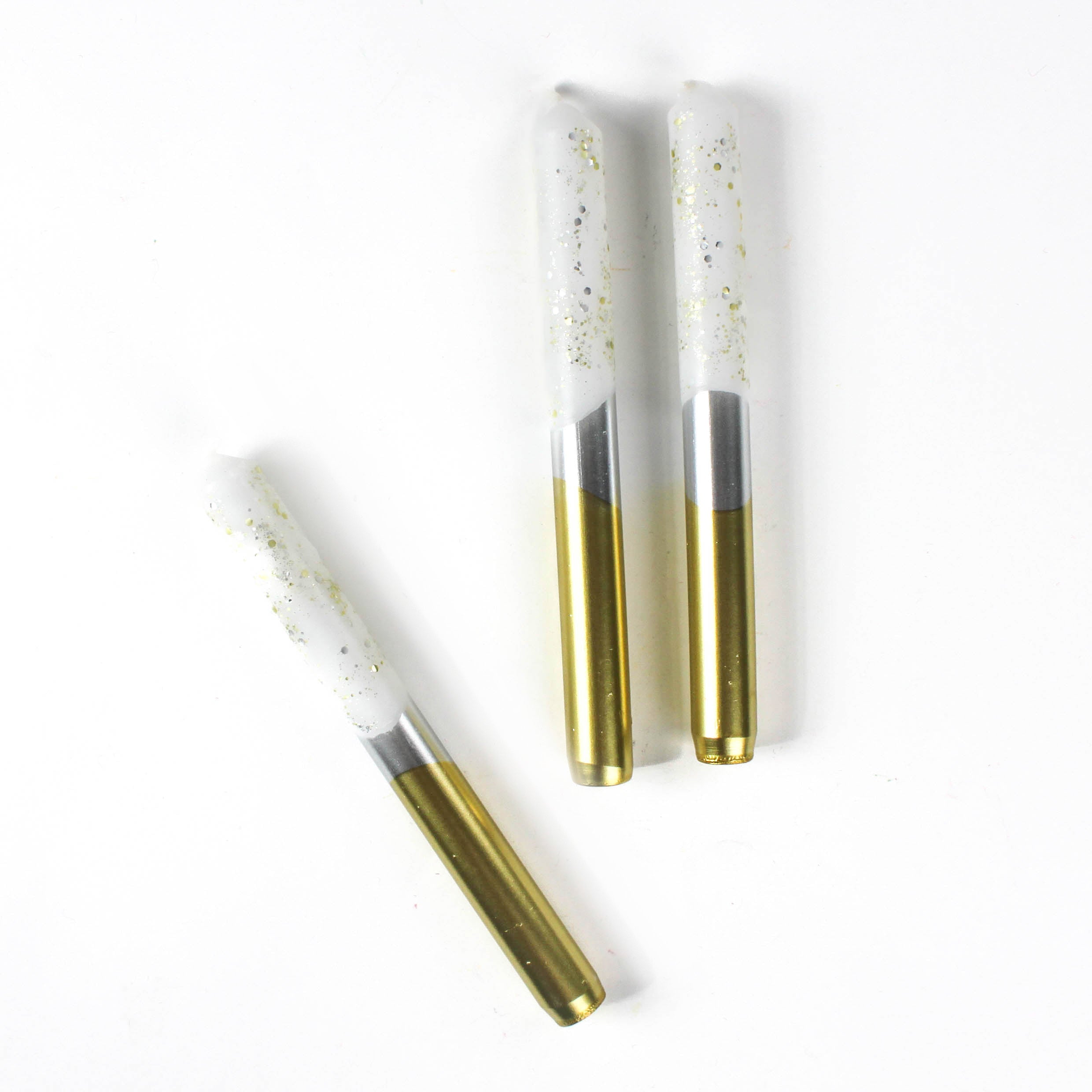 Silver and gold taper candles with glitter accents on the upper part of the candle against a white background. 