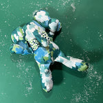 Green and blue patterned stuffed elephant toy with a matching bow in green background.