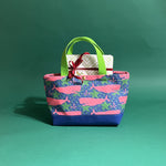 Small Whale of a Time canvas tote bag with lime straps and blue fabric with a repeating pink whale  and green star motif with gifts sticking out of the top.