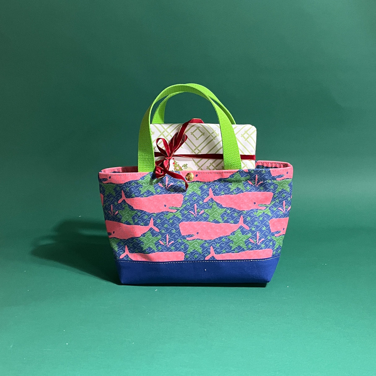 Small Whale of a Time canvas tote bag with lime straps and blue fabric with a repeating pink whale  and green star motif with gifts sticking out of the top.