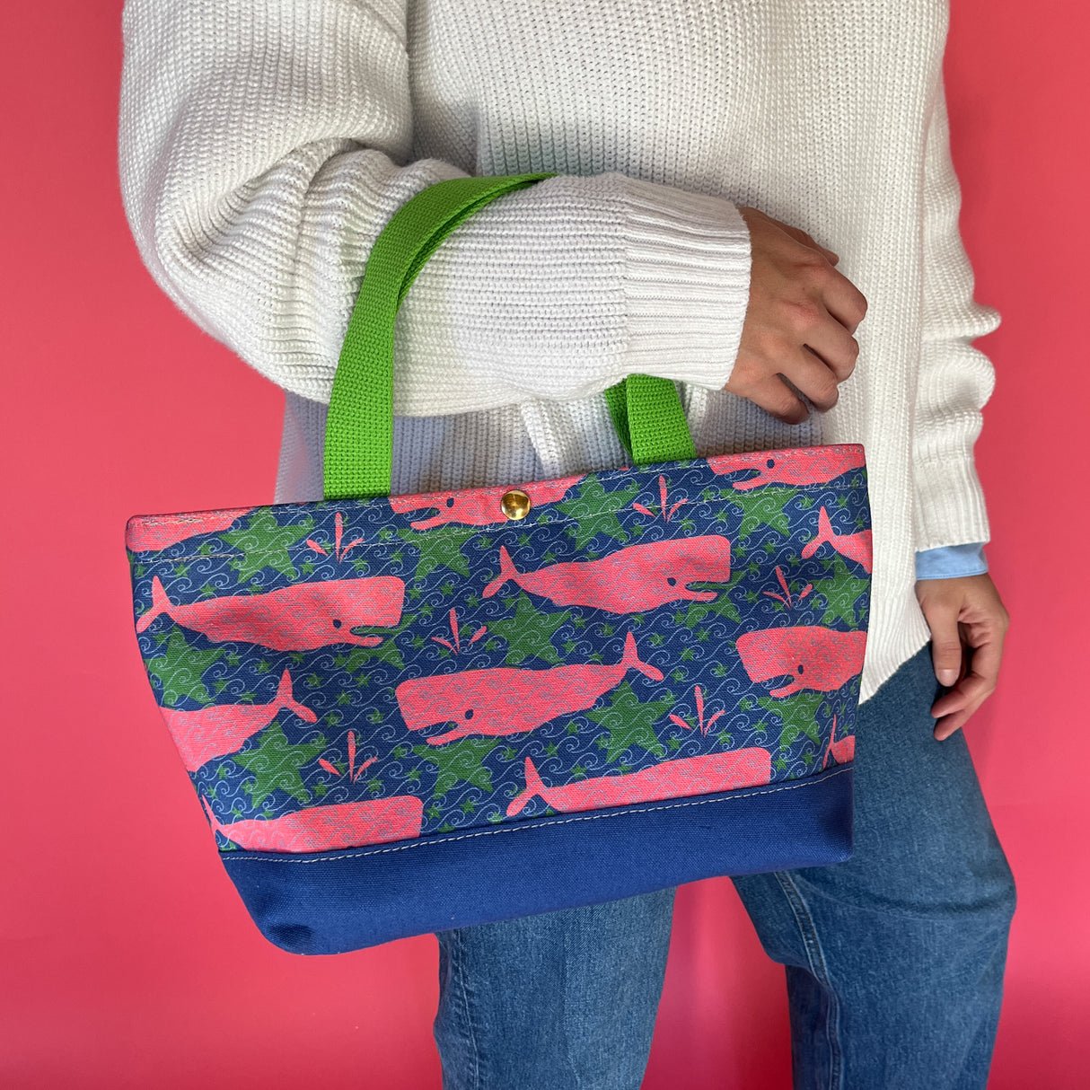 Whale of a Time small canvas tote bag with lime straps and blue fabric with a repeating pink whale  and green star motif on models arm