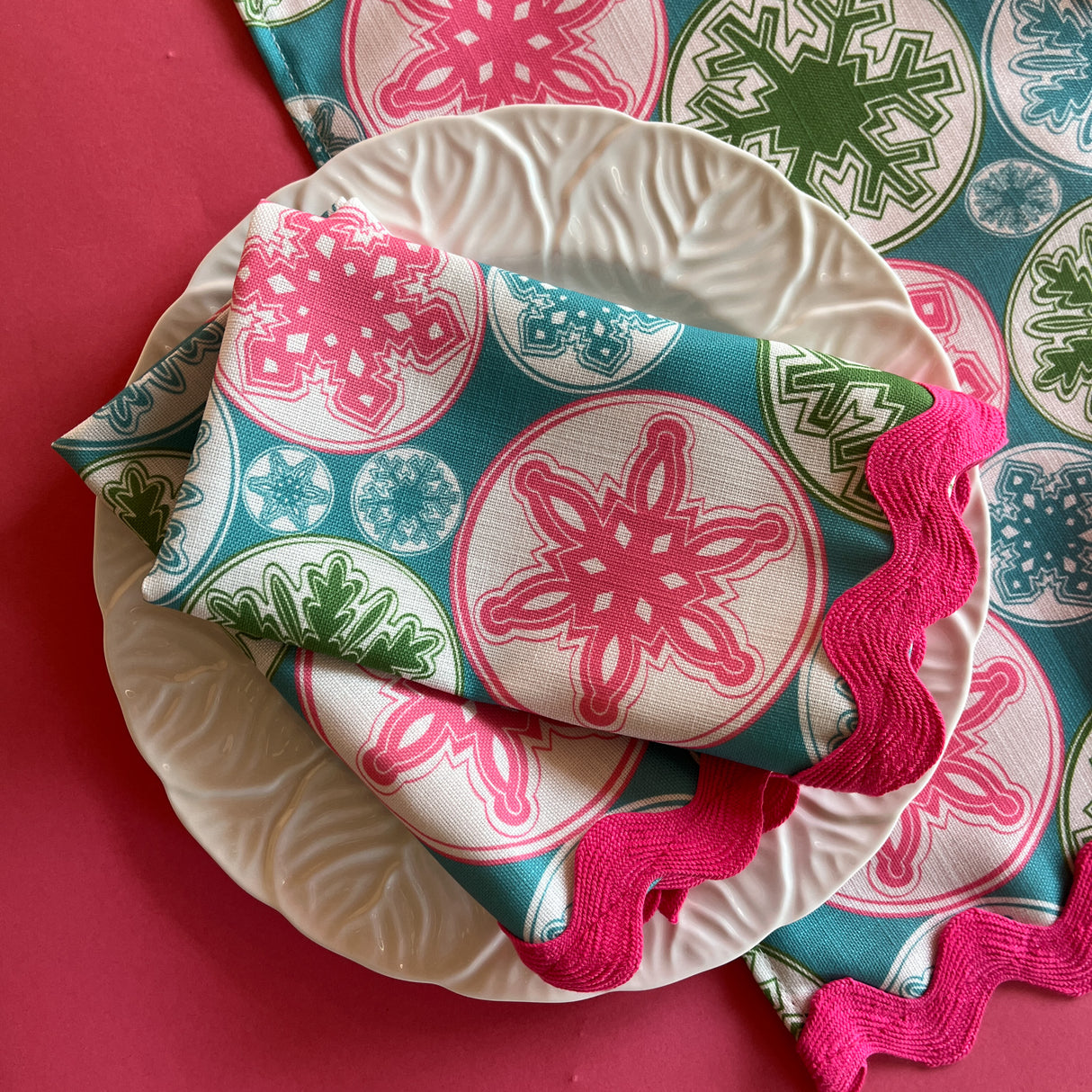 Folded napkins featuring pink snowflakes on a blue background with pink ric rac trim resting on a white plate