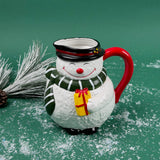 Ceramic snowman-shaped pitcher with a red handle and green scarf on a green background with faux snow and pine accents