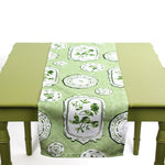 Green and white table runner with decorative plate motifs displayed on a green table.