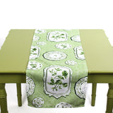 Green and white table runner with decorative plate motifs displayed on a green table.