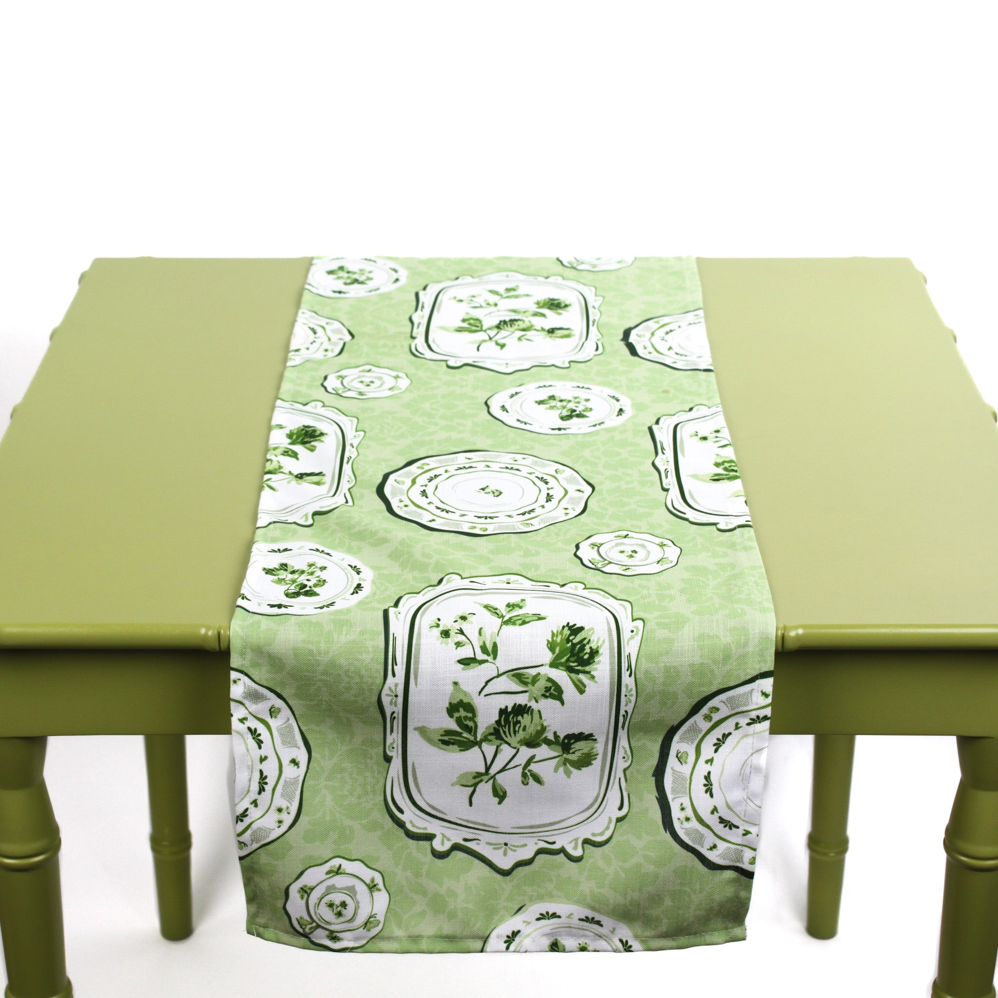 Green and white table runner with decorative plate motifs displayed on a green table.