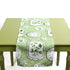 Green and white table runner with decorative plate motifs displayed on a green table.