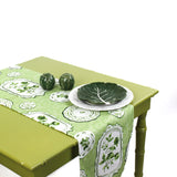 Styled green and white table runner on a green table with decorative plates and ceramic accents.
