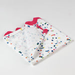 Close-up of folded cloth napkin featuring multicolor confetti dots and pink scalloped trim.