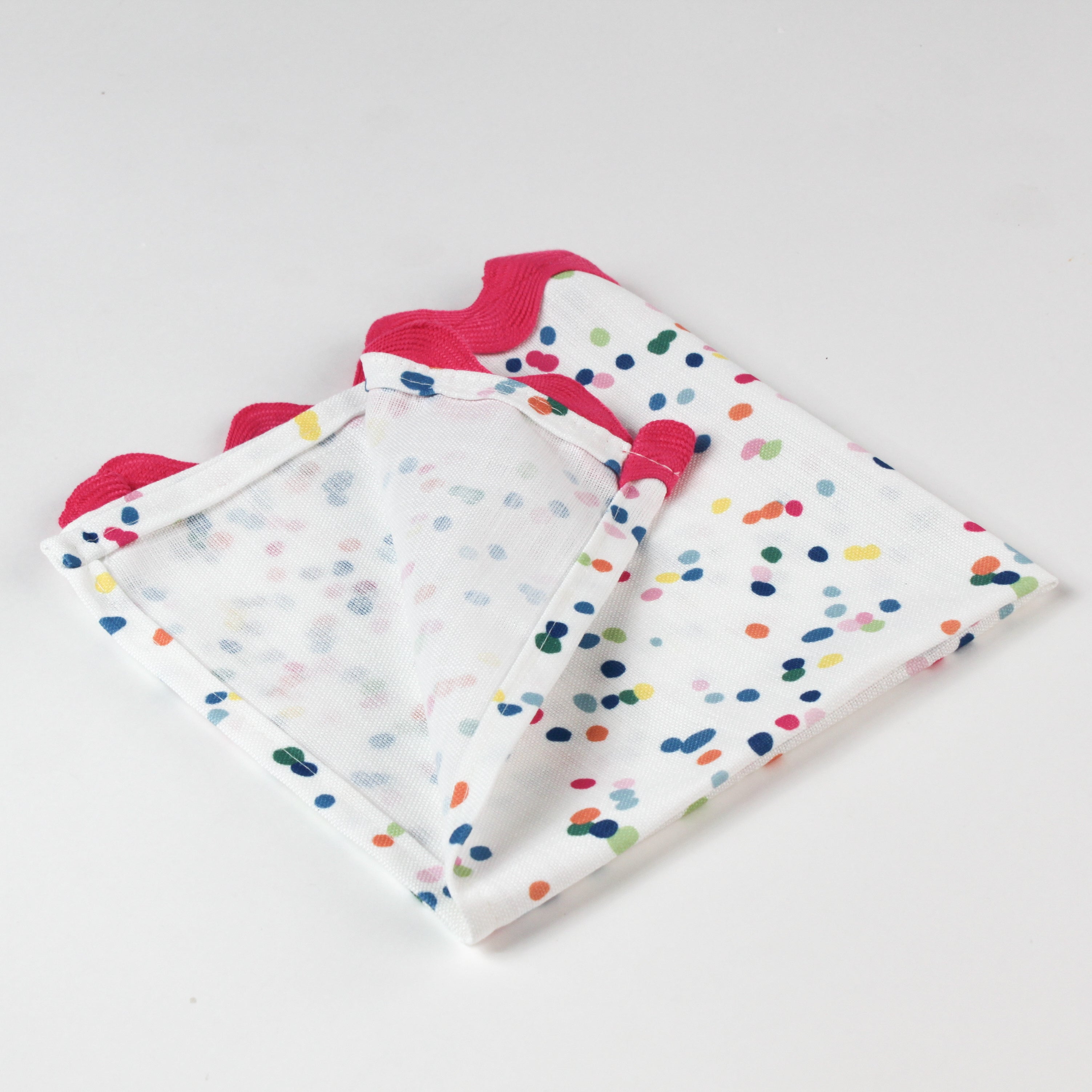 Close-up of folded cloth napkin featuring multicolor confetti dots and pink scalloped trim.