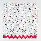 Cloth napkin laid flat with multicolor confetti dots and pink scalloped trim.