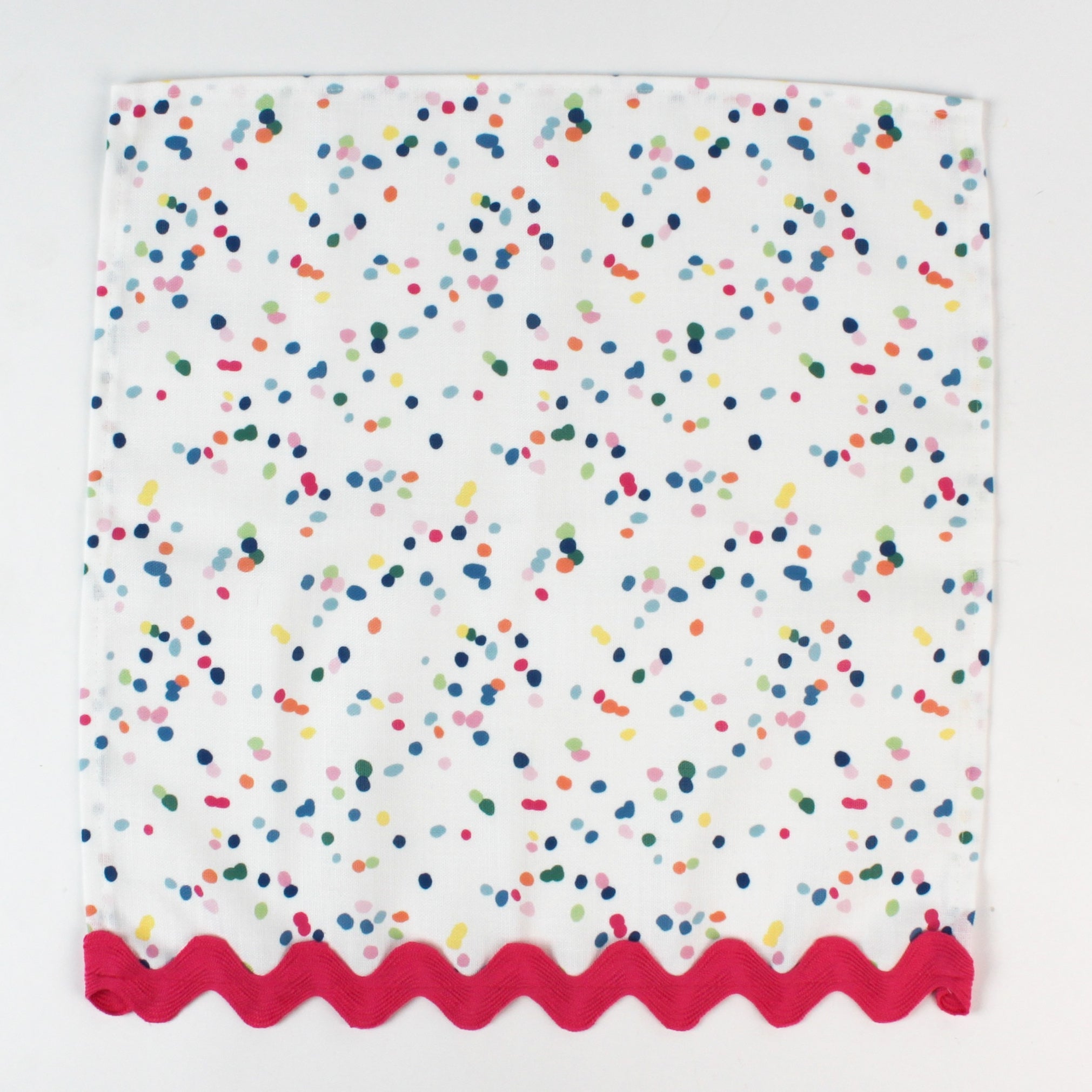 Cloth napkin laid flat with multicolor confetti dots and pink scalloped trim.