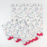 Set of cloth napkins with a colorful confetti dot pattern and pink scalloped trim.