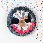 Confetti-patterned cloth napkin placed in a blue bowl with a woven bunny napkin ring.