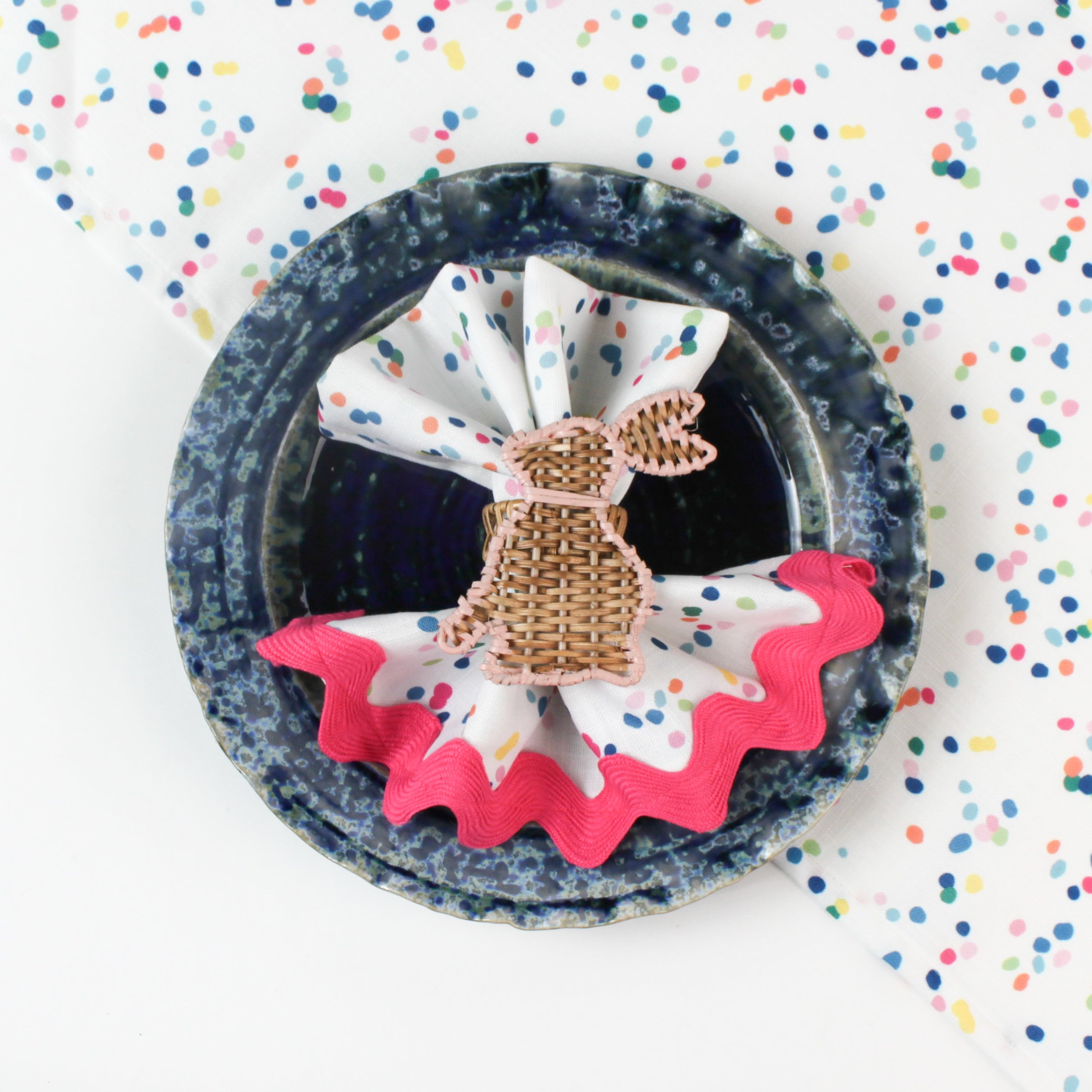 Confetti-patterned cloth napkin placed in a blue bowl with a woven bunny napkin ring.