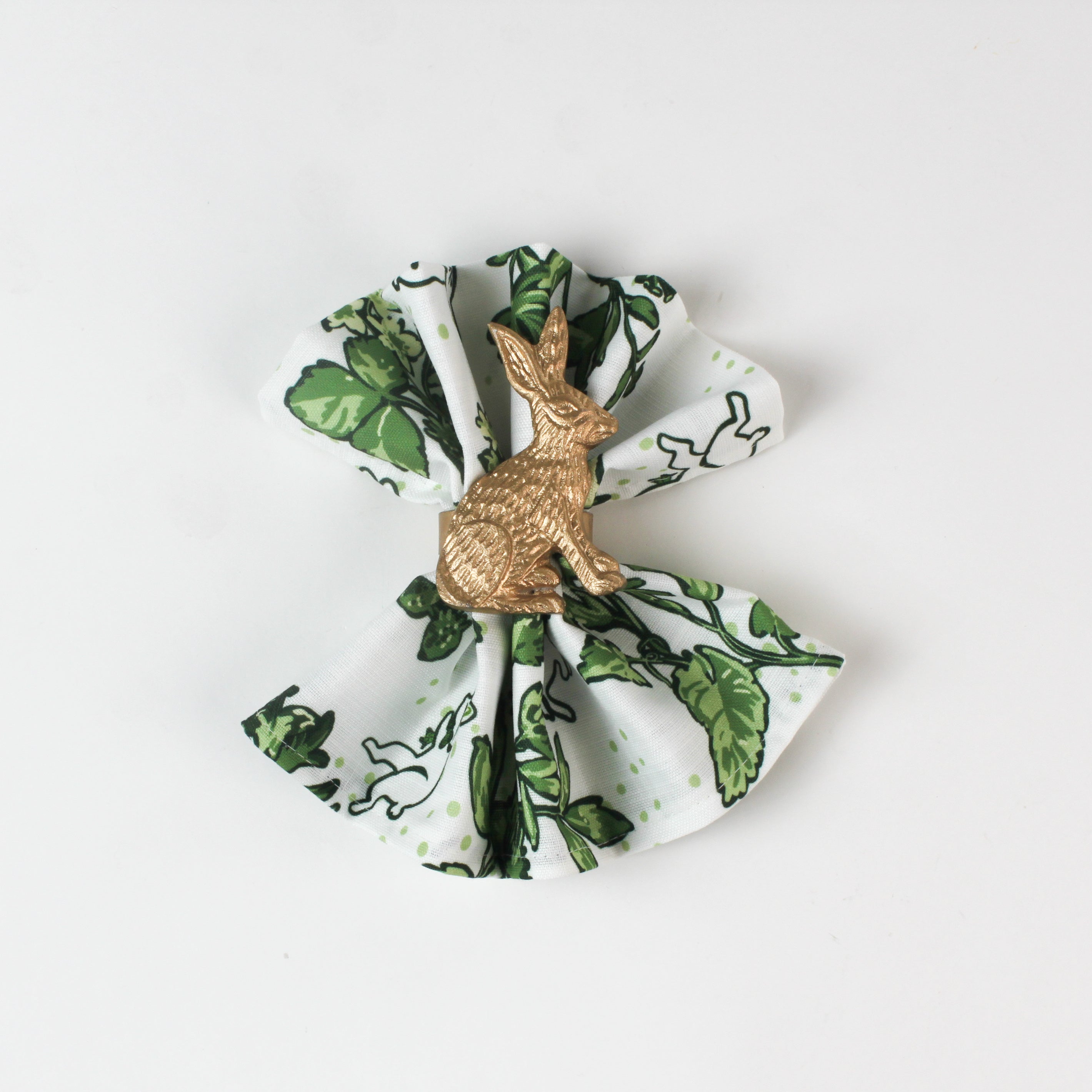 Green botanical patterned cloth napkin styled with a gold rabbit napkin ring.