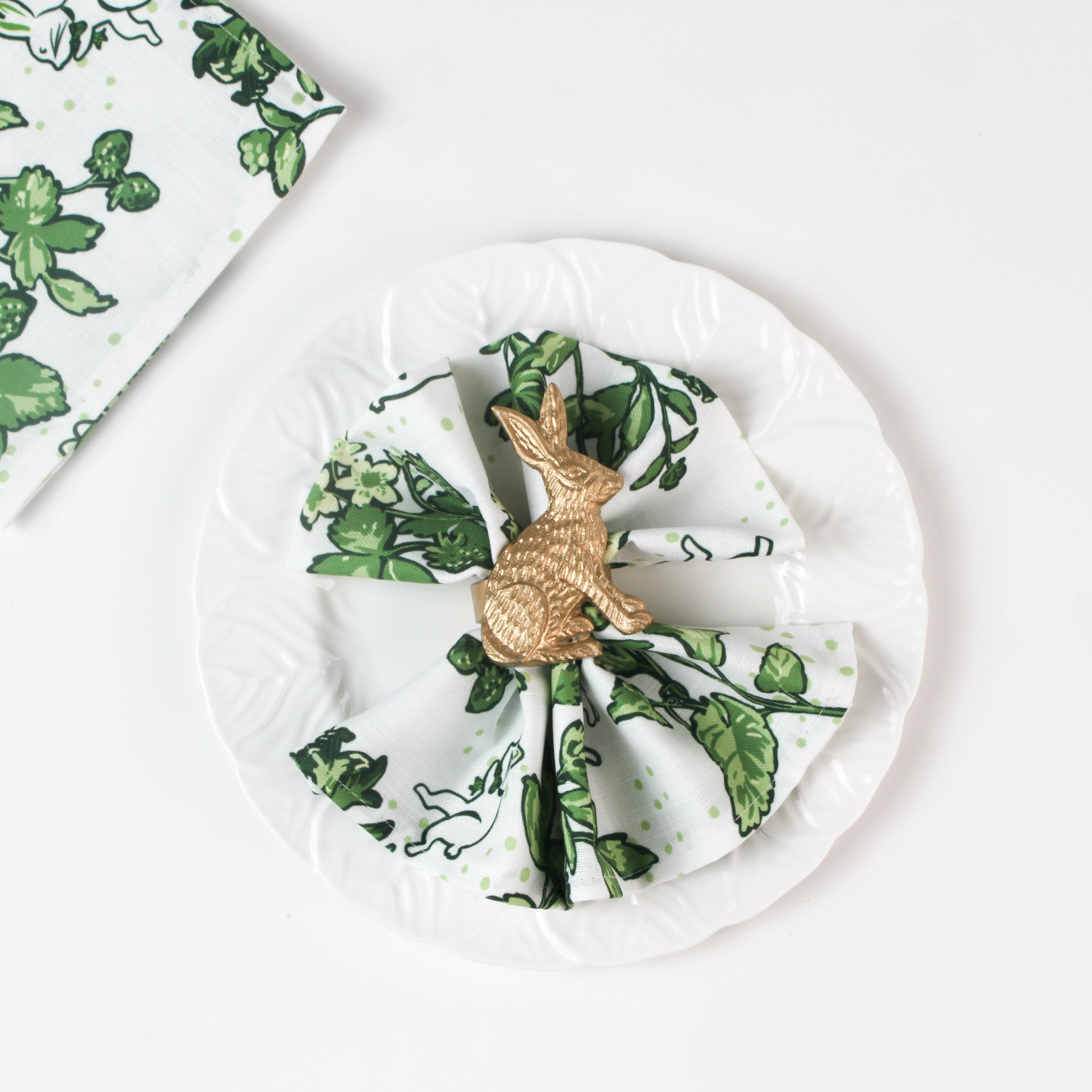 Green botanical  in white plate patterned cloth napkin styled with a gold rabbit napkin ring.