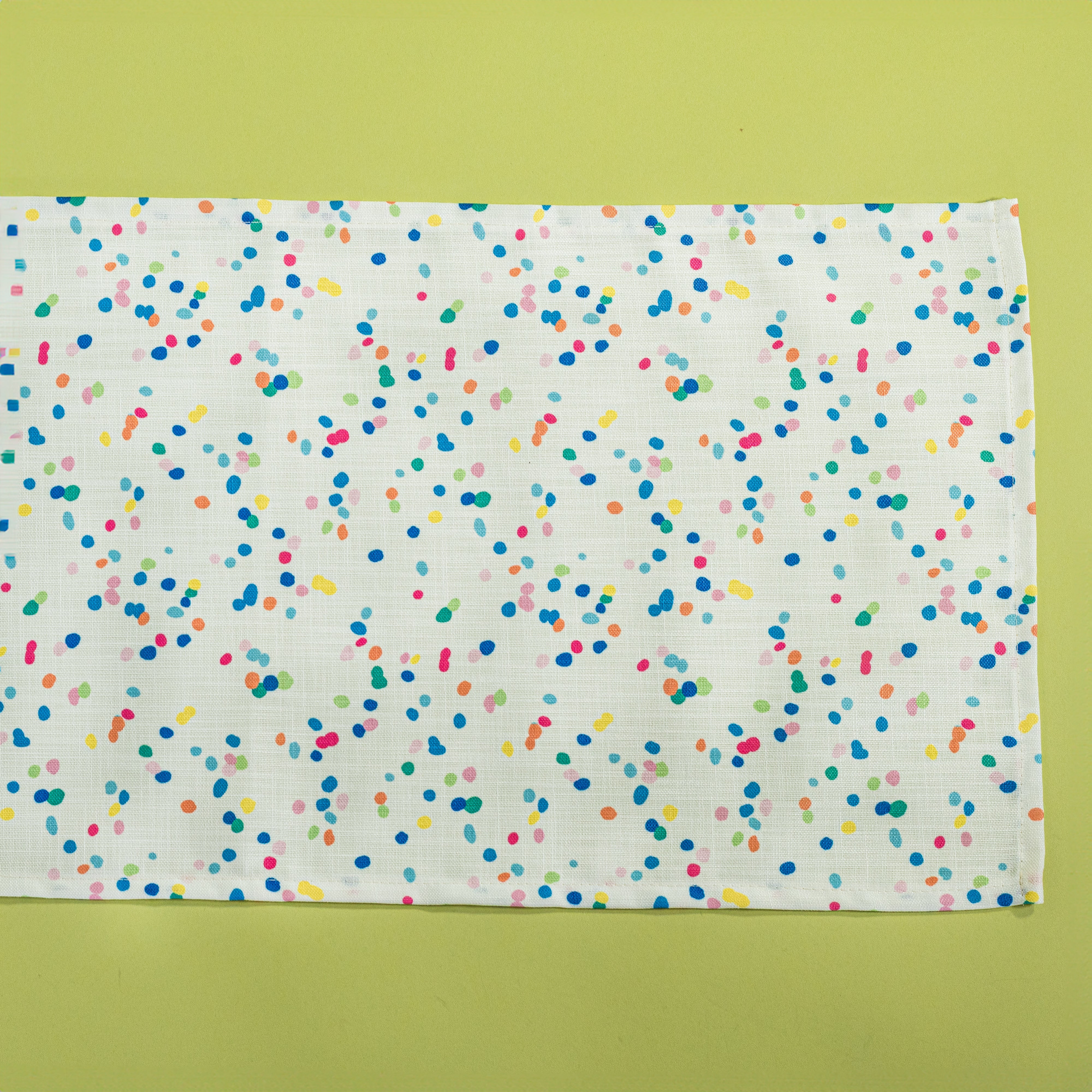 A Springtime confetti print cloth table runner on a light green background
