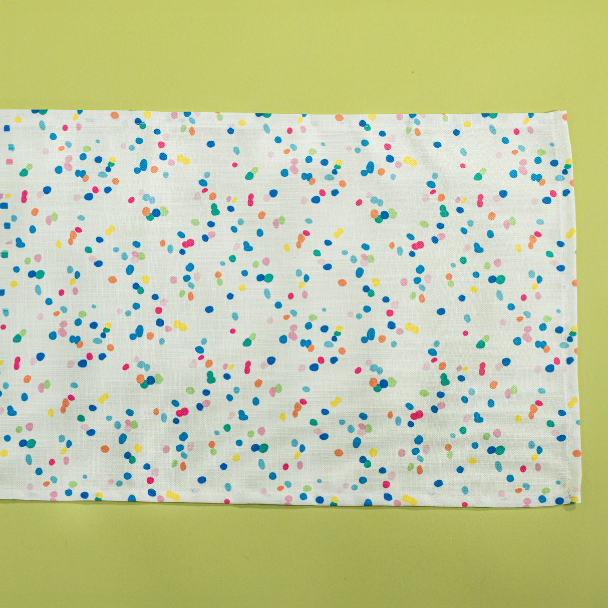 A Springtime confetti print cloth table runner on a light green background