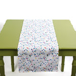 White table runner with colorful confetti-style dots displayed on a green table.