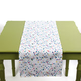 White table runner with colorful confetti-style dots displayed on a green table.
