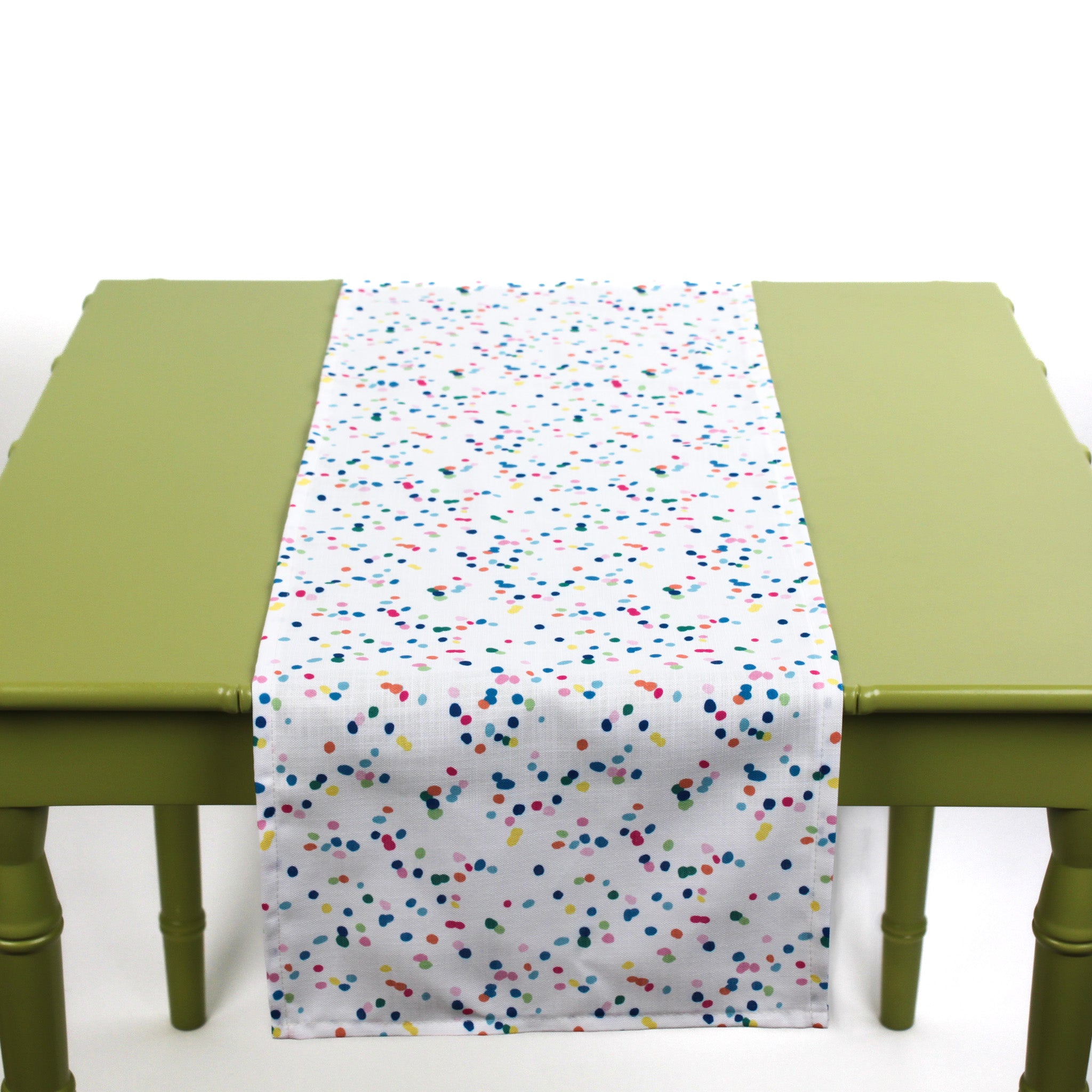 White table runner with colorful confetti-style dots displayed on a green table.