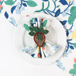 Botanical print cloth napkin styled on a white plate with a woven strawberry napkin ring.